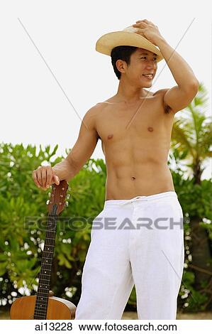 Young man standing, touching hat and leaning on guitar View Large Photo Image Stock Photo - Young man standing, touching hat and leaning on guitar. Fotosearch
