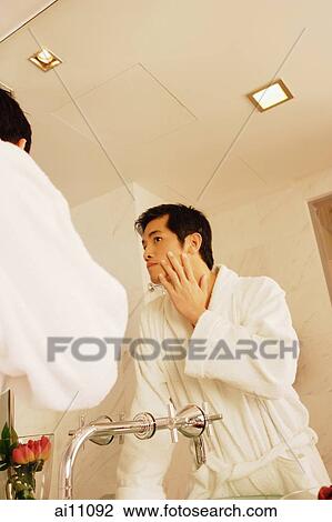 Young man touching his face, looking in mirror View Large Photo Image Stock Image - Young man touching his face, looking in mirror. Fotosearch