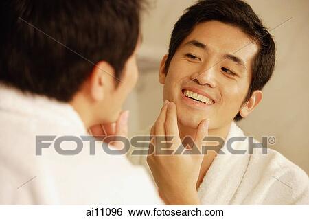 Young man touching his face, looking in mirror View Large Photo Image Stock Photograph - Young man touching his face, looking in mirror. Fotosearch