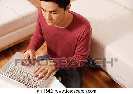 Stock Image - Young man using laptop, high angle view. Fotosearch