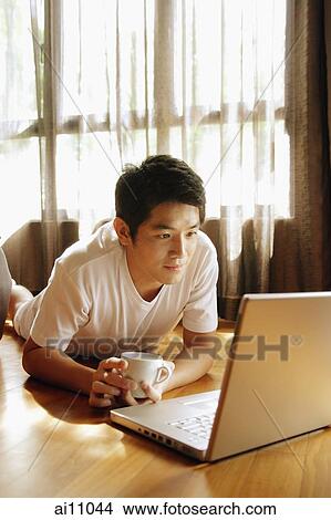 Young man using laptop, lying on floor View Large Photo Image Picture - Young man using laptop, lying on floor. Fotosearch