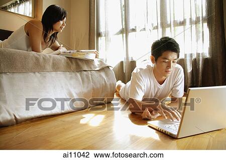 Young man using laptop, young woman lying on bed reading magazine View Large Photo Image Stock Image - Young man using laptop, young woman lying on bed reading magazine. Fotosearch