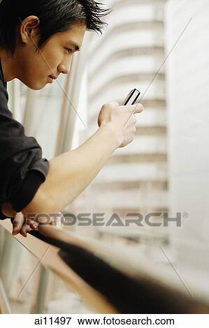 Stock Photo - Young man using mobile phone, sideview. Fotosearch