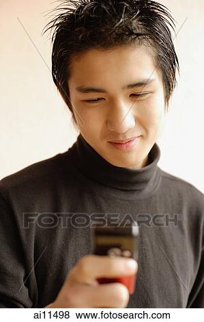 Stock Photo - Young man using mobile phone, smiling. Fotosearch