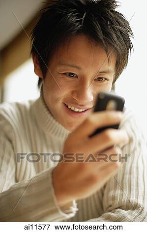 Stock Photo - Young man using mobile phone, smiling. Fotosearch