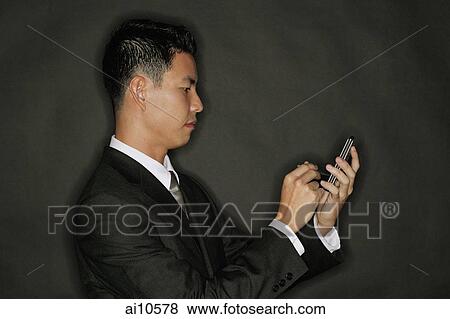 Stock Photo - Young man using PDA, standing in profile. Fotosearch