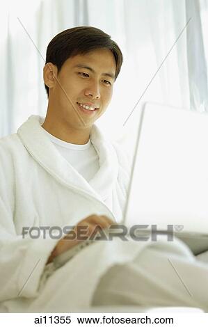 Stock Photography - Young man wearing robe, using laptop. Fotosearch