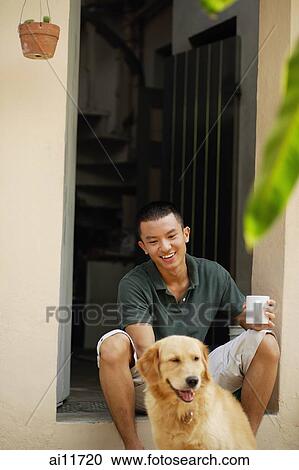 Stock Image - Young man with dog, sitting at doorway. Fotosearch