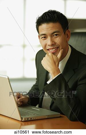 Stock Image - Young man with hand on chin, looking at camera, toothy smile. Fotosearch