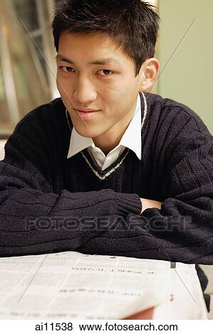Stock Photo - Young man with newspaper open in front of him, looking at camera. Fotosearch