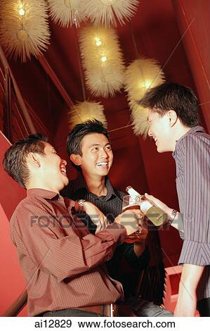Young men in night club holding out drinks, laughing View Large Photo Image Stock Photo - Young men in night club holding out drinks, laughing. Fotosearch