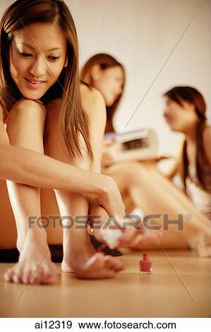 Stock Photo -  Young woman applying nail polish, friends in the background. Fotosearch