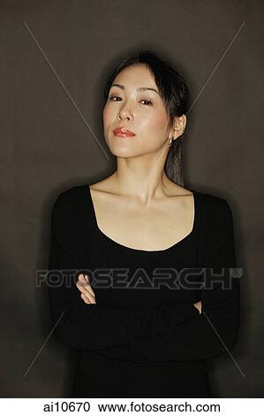 Young woman, arms crossed, standing against a black background View Large Photo Image Stock Image - Young woman, arms crossed, standing against a black background. Fotosearch