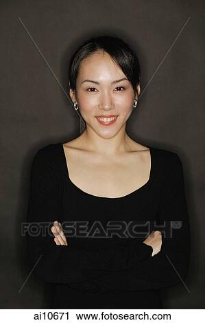 Young woman, arms crossed, standing against a black background View Large Photo Image Stock Image - Young woman, arms crossed, standing against a black background. Fotosearch