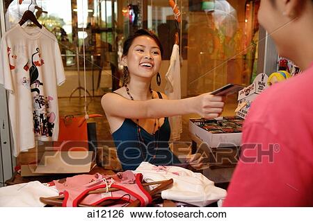 Young woman at shop counter, making a purchase View Large Photo Image Stock Photograph - Young woman at shop counter, making a purchase. Fotosearch