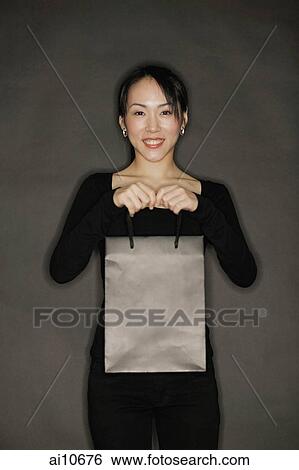 Stock Photograph - Young woman carrying shopping bag, black background. Fotosearch