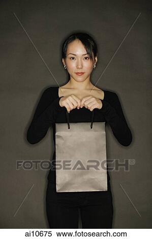 Stock Photography - Young woman carrying shopping bag, black background. Fotosearch