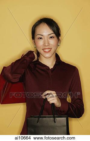 Young woman carrying shopping bags, yellow background View Large Photo Image Picture - Young woman carrying shopping bags, yellow background. Fotosearch