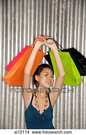 Young woman carrying shopping bags over her head, smiling at camera View Large Photo Image Picture - Young woman carrying shopping bags over her head, smiling at camera. Fotosearch