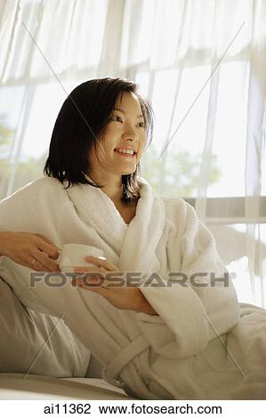 Stock Image - Young woman drinking coffee, looking away. Fotosearch