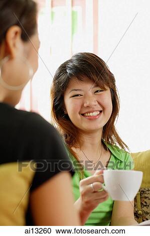 Young woman facing another woman, holding teacup View Large Photo Image Stock Image - Young woman facing another woman, holding teacup. Fotosearch