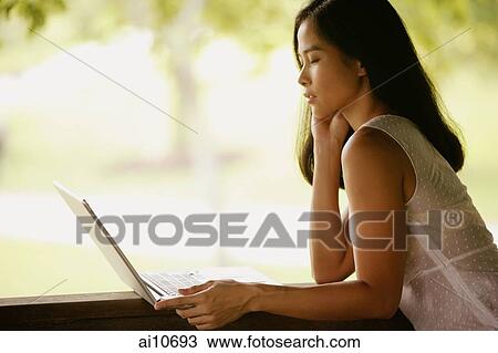 Young woman, hand on chin, looking at laptop View Large Photo Image Stock Image - Young woman, hand on chin, looking at laptop. Fotosearch