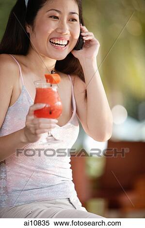 Stock Photography - Young woman holding a drink and using mobile phone. Fotosearch