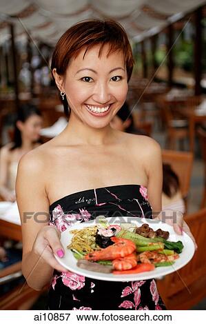 Young woman holding a plate of food, looking at camera View Large Photo Image Stock Photo - Young woman holding a plate of food, looking at camera. Fotosearch
