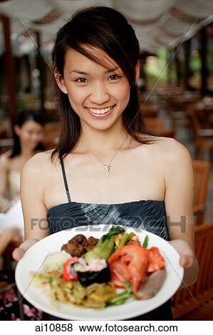 Stock Photo - Young woman holding a plate of food, looking at camera. Fotosearch