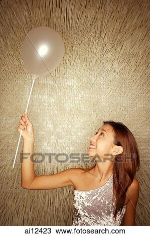 Stock Image - Young woman holding balloon, looking up. Fotosearch