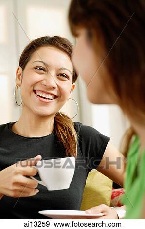 Young woman holding cup and saucer, smiling at another woman facing her View Large Photo Image Stock Photo - Young woman holding cup and saucer, smiling at another woman facing her. Fotosearch