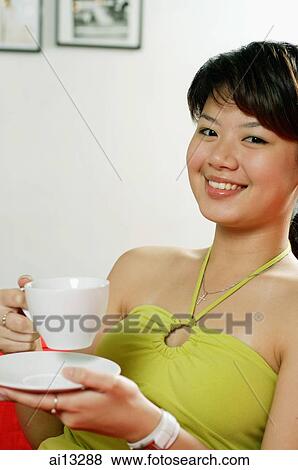 Young woman holding cup and saucer, looking at camera, smiling View Large Photo Image Stock Photo - Young woman holding cup and saucer, looking at camera, smiling. Fotosearch