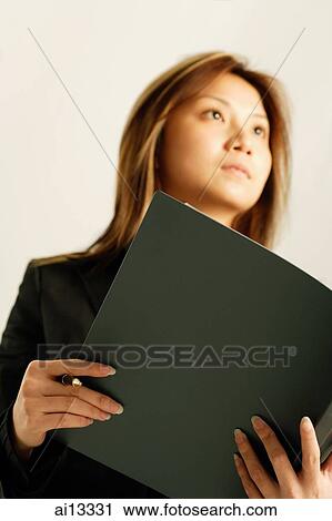 Stock Image - Young woman, holding file, looking away. Fotosearch
