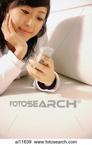 Stock Photo - Young woman holding mobile phone, hand on chin. Fotosearch