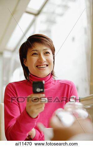 Young woman holding mobile phone, facing another person View Large Photo Image Stock Image - Young woman holding mobile phone, facing another person. Fotosearch