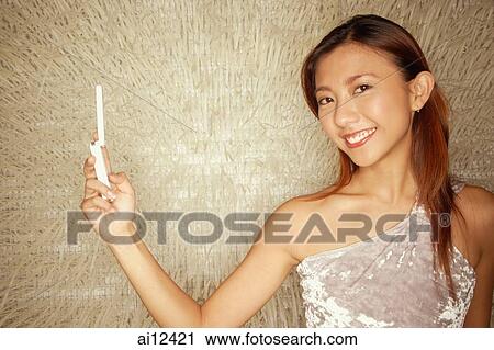 Stock Image - Young woman holding mobile phone, looking at camera. Fotosearch