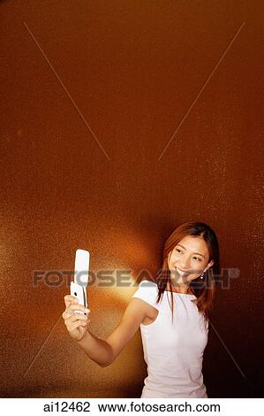 Stock Image - Young woman holding mobile phone, smiling. Fotosearch
