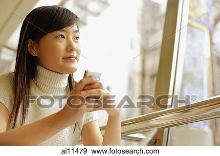 Young woman holding mobile phone, looking away View Large Photo Image Stock Photo - Young woman holding mobile phone, looking away. Fotosearch