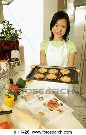 Young woman holding out baking tray, looking at camera View Large Photo Image Stock Photograph - Young woman holding out baking tray, looking at camera. Fotosearch