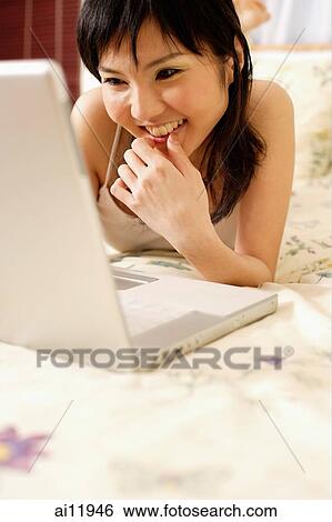 Young woman in bedroom using laptop View Large Photo Image Stock Photograph - Young woman in bedroom using laptop. Fotosearch