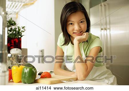 Young woman in kitchen, hand on chin, looking at camera View Large Photo Image Picture - Young woman in kitchen, hand on chin, looking at camera. Fotosearch