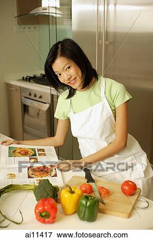 Young woman in kitchen with cookbook, looking at camera View Large Photo Image Stock Photo - Young woman in kitchen with cookbook, looking at camera. Fotosearch