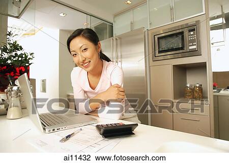 Young woman in kitchen, with laptop and calculator, looking at camera View Large Photo Image Stock Image - Young woman in kitchen, with laptop and calculator, looking at camera. Fotosearch