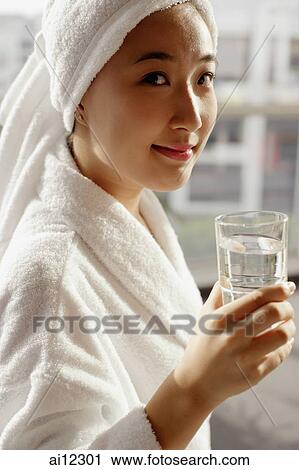 Stock Image -  Young woman in robe holding glass of water. Fotosearch