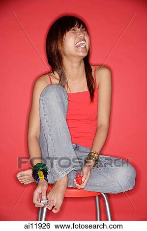 Stock Photograph - Young woman laughing, holding nail polish. Fotosearch