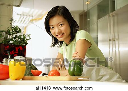 Stock Image - Young woman leaning on kitchen counter, looking at camera. Fotosearch