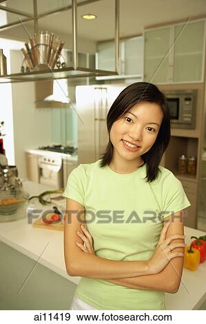 Stock Photo - Young woman leaning on kitchen counter, arms crossed, looking at camera. Fotosearch