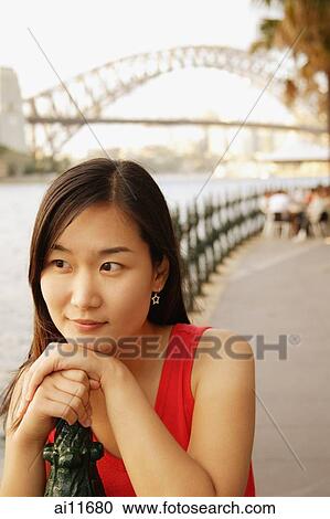Stock Image - Young woman leaning on railing, looking away. Fotosearch