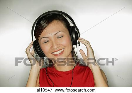 Stock Photo - Young woman listening to headphones, smiling. Fotosearch