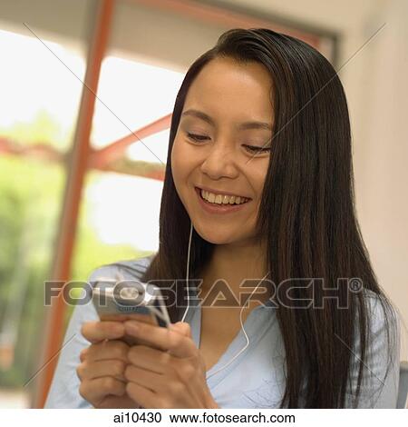 Stock Image - Young woman listening to personal stereo. Fotosearch